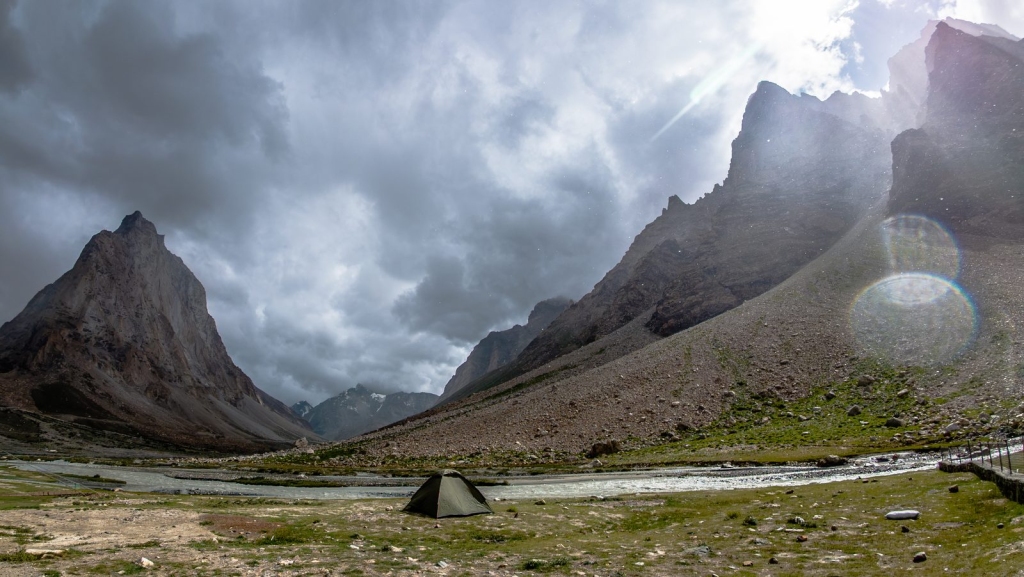Small green tent pitched by the river below Gonbo Rangjon under stormy clouds