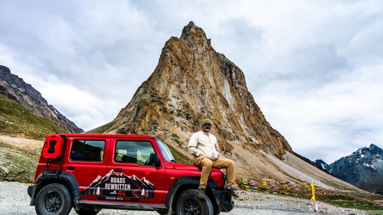 Alok sitting on the red Suzuki Jimny in front of Gonbo Rangjon peak in Zanskar