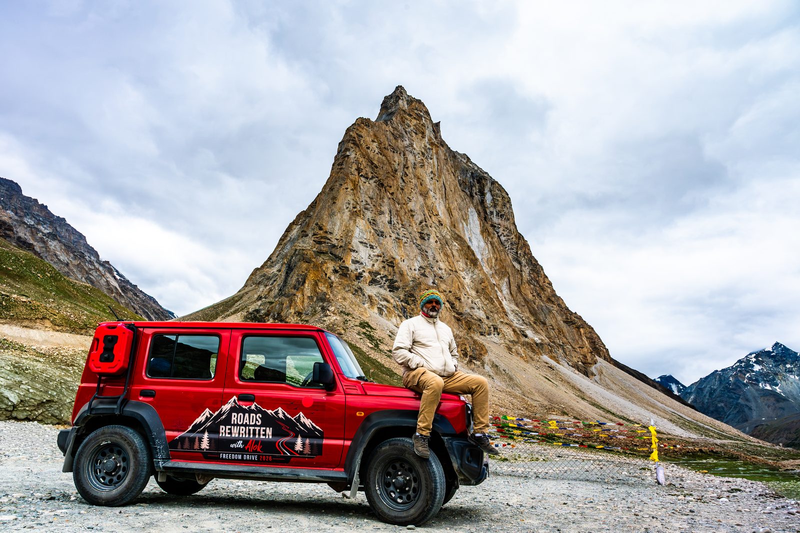 Alok sitting on the red Suzuki Jimny in front of Gonbo Rangjon peak in Zanskar