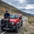 Alok Brahmbhatt sitting on the hood of a red Jimny on a mountain road during Freedom Drive Part 1