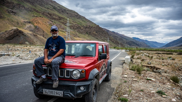 Alok Brahmbhatt sitting on the hood of a red Jimny on a mountain road during Freedom Drive Part 1