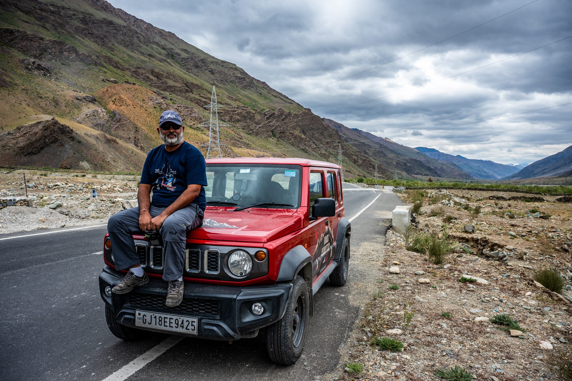Alok Brahmbhatt sitting on the hood of a red Jimny on a mountain road during Freedom Drive Part 1