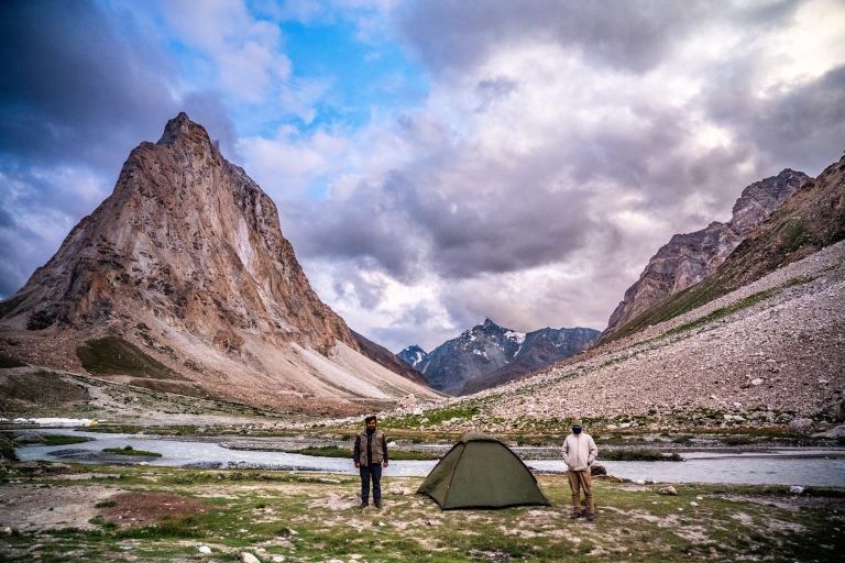 Two travellers standing by a tent at Rashil village campsite in Lahaul with mountains in the background