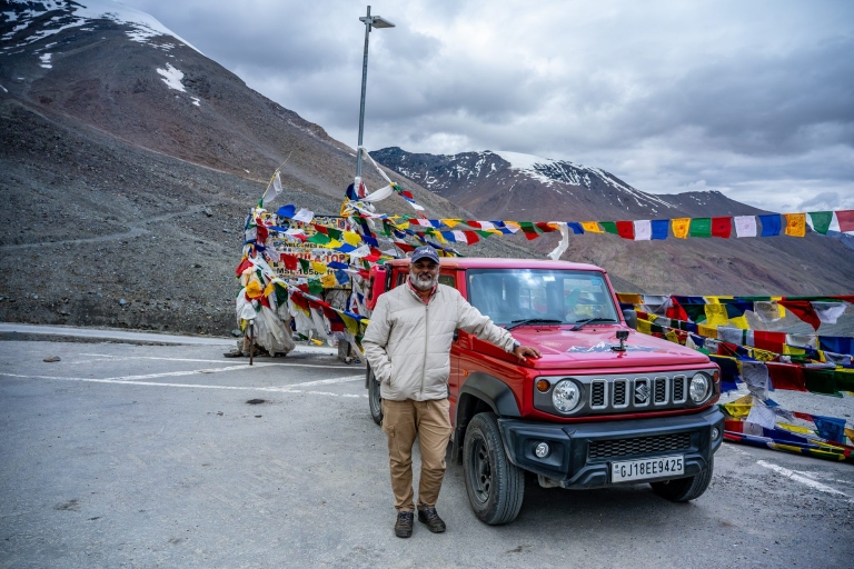 Red Suzuki Jimny parked at Shinkula Top signpost, 16500 feet, with prayer flags