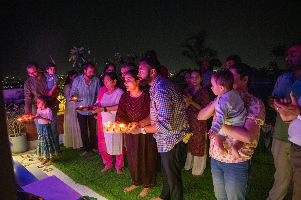 Family performing Janmashtami aarti with diyas on the rooftop at night