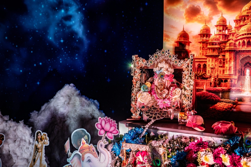 Close-up of the decorated Laddu Gopal idol on a floral jhula for Janmashtami, with a Vrindavan palace backdrop