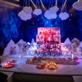 Janmashtami decoration at home with cotton-cloud mountains, cutouts of gopis and elephants, and a Laddu Gopal jhula against a Vrindavan palace backdrop