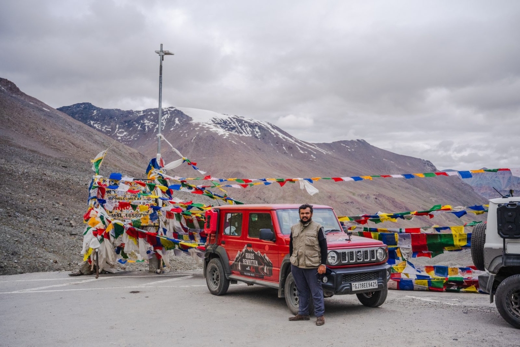 Red Suzuki Jimny with prayer flags at a high mountain pass
