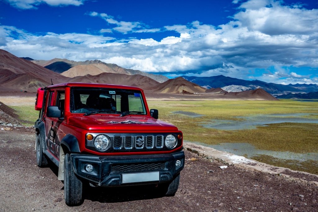 Red Suzuki Jimny parked beside a high-altitude lake in Ladakh